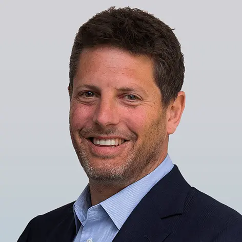 Headshot of Mark Serry, a professional with short, dark hair, wearing a suit jacket and a light blue shirt, smiling at the camera.